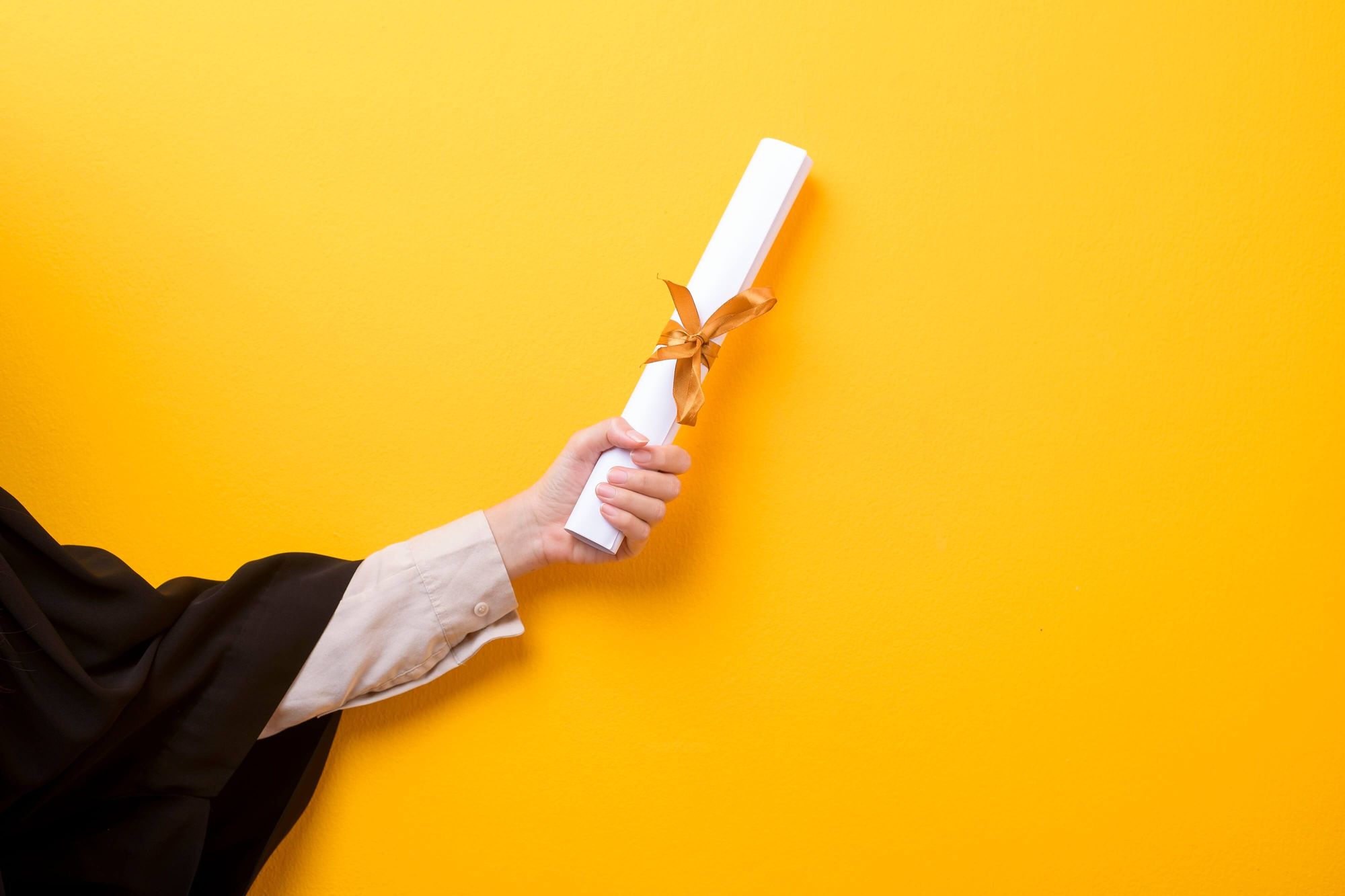 Yellow background with someones arm holding a degree (attain a degree or obtain a degree?)