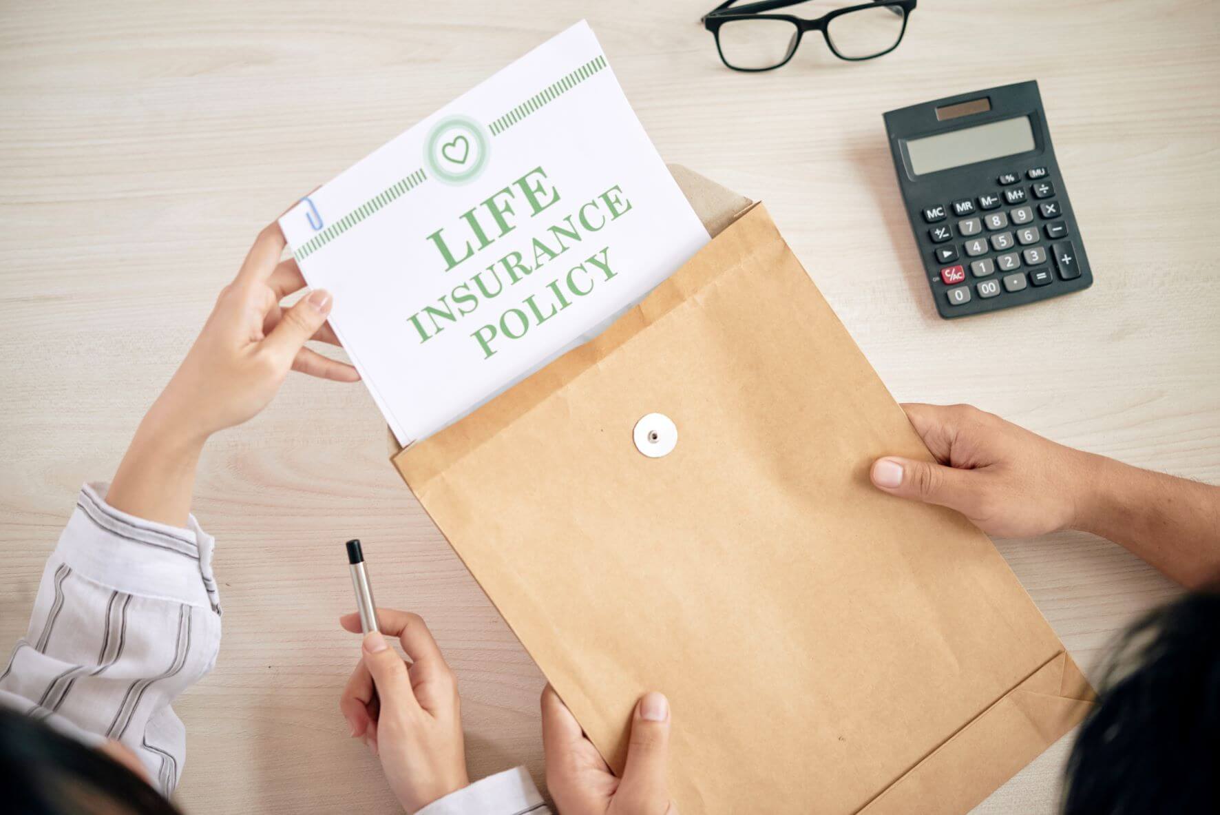 Close up photo of two pairs of hands holding a folder and removing paper that reads "life insurance policy."